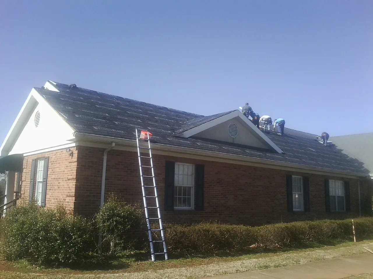 Crew tearing shingles off a brick ranch roof with a ladder set — Emergency Roof Repair work by our crew in Delafield