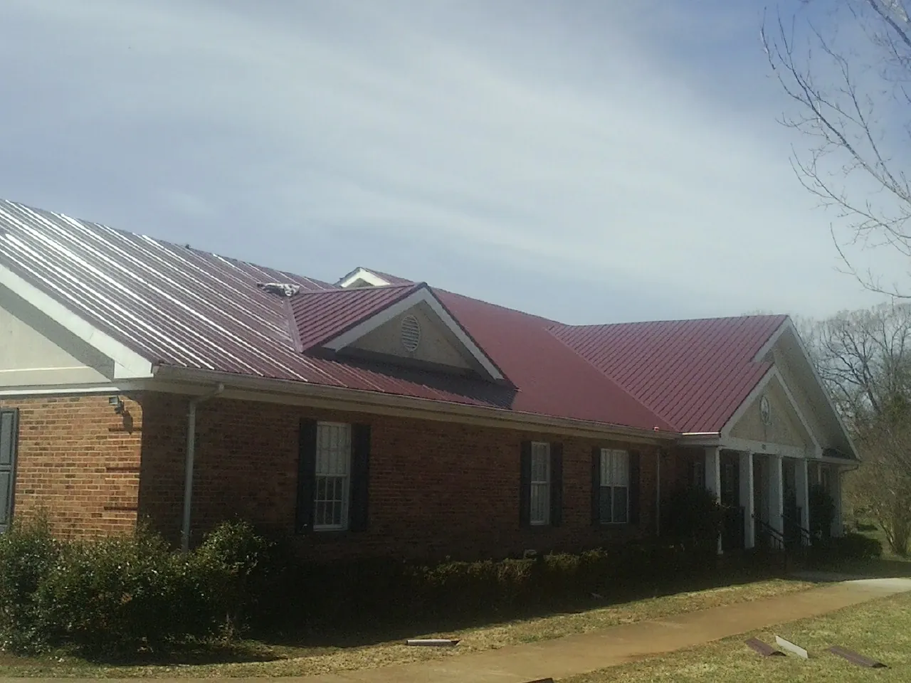 Red metal roof with gabled entries on a long brick building, from a Hail Damage Roof Repair job in Delafield