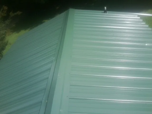 New green metal panels meeting at the ridge of a roof — Flat Roof Repair work by our crew in Delafield