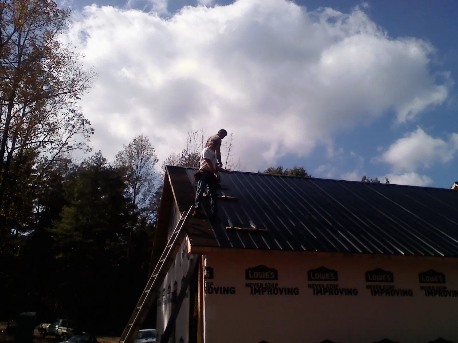 Roofer fastening dark metal panels high against a cloudy sky, from a Roof Inspection job in Delafield